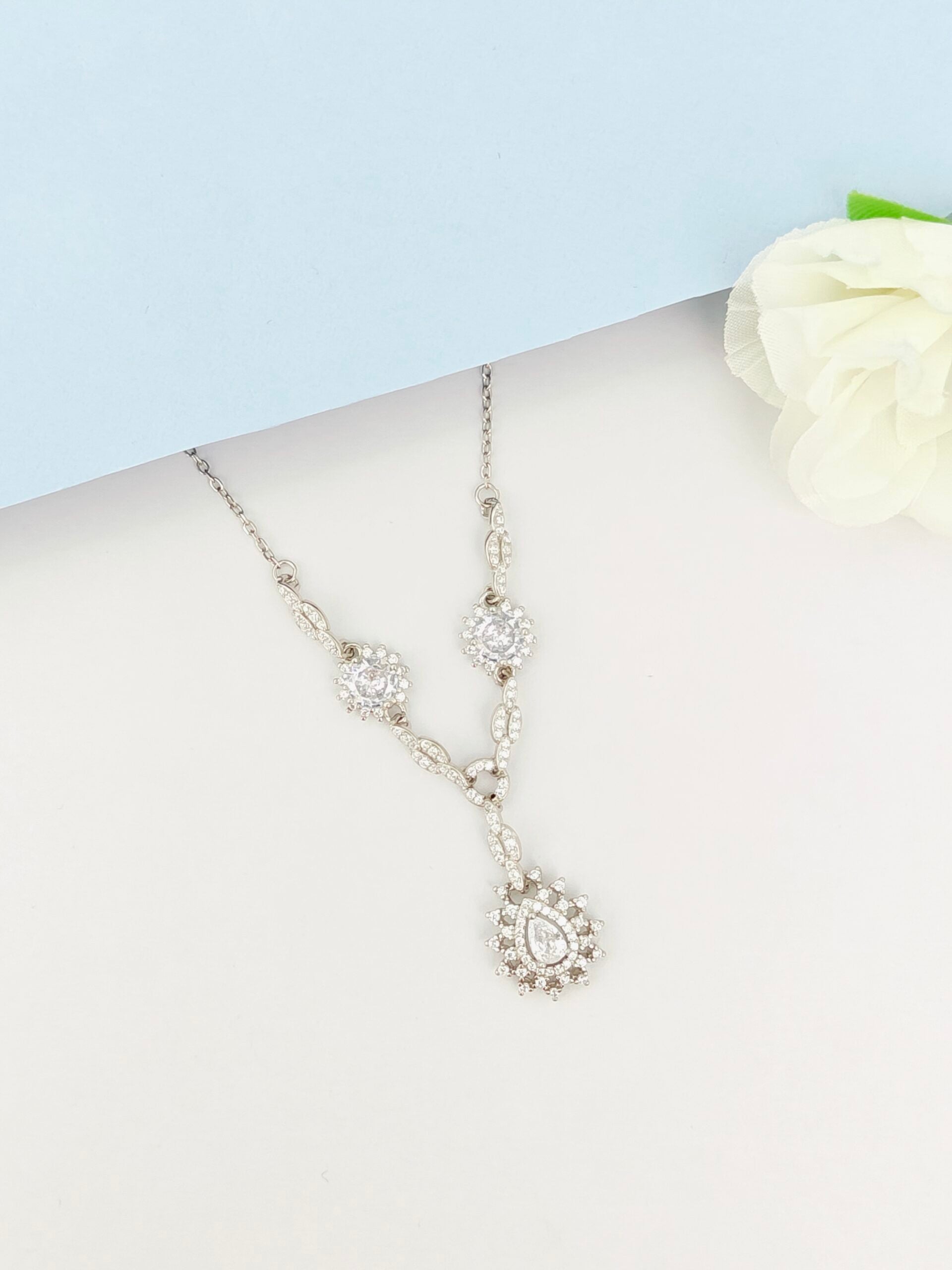 Silver necklace with floral elements on a mannequin bust against a light blue background